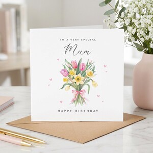 May include: A white greeting card with the text "TO A VERY SPECIAL Mum HAPPY BIRTHDAY". The card features a watercolor bouquet of pink and yellow flowers tied with a pink ribbon, and small pink hearts.