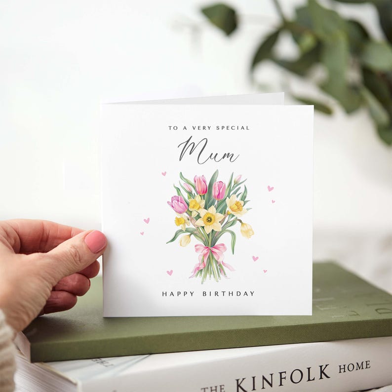 May include: A white greeting card with the text "TO A VERY SPECIAL Mum HAPPY BIRTHDAY". The card features a watercolor bouquet of pink tulips, yellow daffodils, and a pink ribbon. Small pink hearts are scattered around the text.