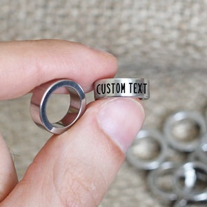 May include: Two silver metal rings, one with the text "CUSTOM TEXT" engraved on it. The rings are about 1 inch in diameter.