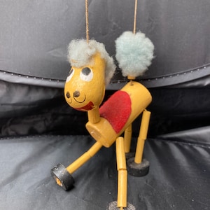 Puede incluir: Un títere de madera de un caballo con una silla de montar roja, pelo azul y ruedas negras. El títere está hecho de madera y tiene una cara pintada.