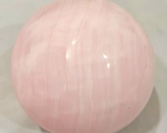 Könnte beinhalten: Eine rosa Selenitkugel mit einer glatten, polierten Oberfläche und einem weißen, gestreiften Muster.