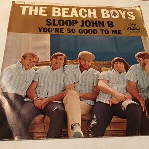 May include: A vintage 45 RPM record sleeve featuring The Beach Boys. The cover art shows the band members sitting on a couch, wearing striped shirts. The title of the record is "Sloop John B" and the B-side is "You're So Good To Me".
