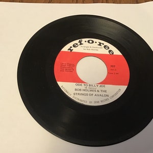 May include: A black vinyl record with a red label. The label has the text "ref･o･ree" and "ODE TO BILLY JOE (B. Gentry) BOB HOLMES & THE STRINGS OF AVALON" along with the song's information, "707 707-A Time 2:44". The label also includes the text "Nationally Distributed by SPAR Record Corporation".
