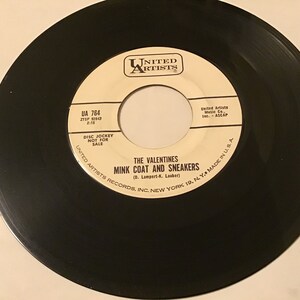 May include: A black vinyl record with a white label. The label has the text "United Artists" in a circle at the top. The text "UA 764" is in the upper left corner. The text "ZTSP 82543" is below "UA 764". The text "2:15" is below "ZTSP 82543". The text "Disc Jockey Not For Sale" is in the center of the label. The text "The Valentines Mink Coat And Sneakers (D. Lampert-K. Lauber)" is in the center of the label. The text "United Artists Records, Inc. New York 10, N.Y. Made in U.S.A." is at the bottom of the label.