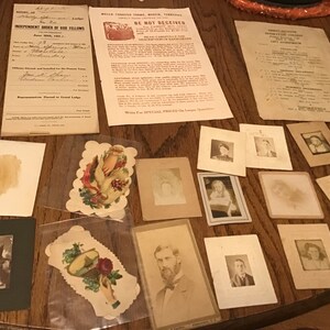 May include: A collection of vintage photographs and paper ephemera, including a framed photo of two children, a framed photo of a man with a beard, and a paper cutout of a hand holding a rose.