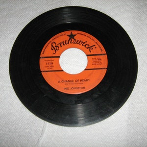 May include: A black vinyl record with an orange label. The label says "Brunswick" and "A Change of Heart" by Inez Johnston. The record number is 55218.