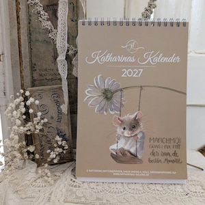 Könnte beinhalten: Ein spiralgebundener Wandkalender für 2027 mit beigem Einband, der eine Maus auf einer Schaukel an einer großen weißen Margerite zeigt. Der Text lautet Katharinas Kalender 2027 und enthält unten deutschen Text sowie Kontaktinformationen.