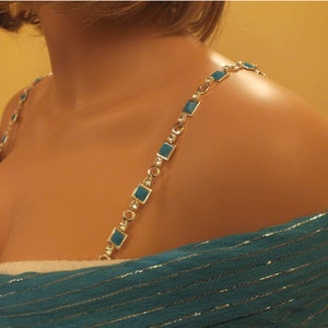 May include: A turquoise and silver bra strap with square-shaped turquoise stones. The strap is shown on a mannequin.