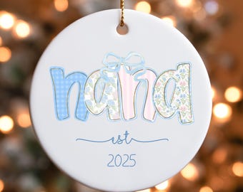 May include: White ceramic ornament with the word "nana" in blue gingham, pink stripes, and floral patterns. The ornament includes the text "est 2025" in a script font, and a gold string for hanging.