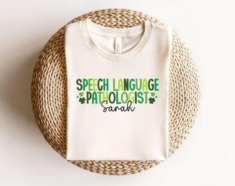 May include: A white t-shirt with green shamrock accents and the text "Speech Language Pathologist Sarah".