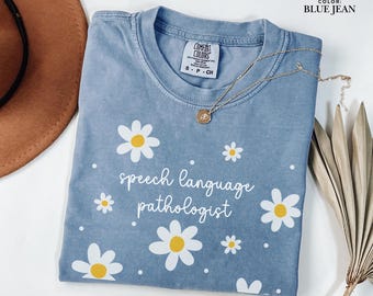 May include: A light blue t-shirt with a daisy print and the text "speech language pathologist" in white. The shirt has a distressed look and is made of a soft, comfortable fabric.