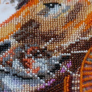 K&ouml;nnte beinhalten: Nahaufnahme eines Perlenbildes, das einen Fuchs mit orangefarbenen, braunen und wei&szlig;en Perlen darstellt. Das Gesicht des Fuchses ist scharf, der Hintergrund ist ein verschwommener Bereich aus orangefarbenen und braunen Perlen.