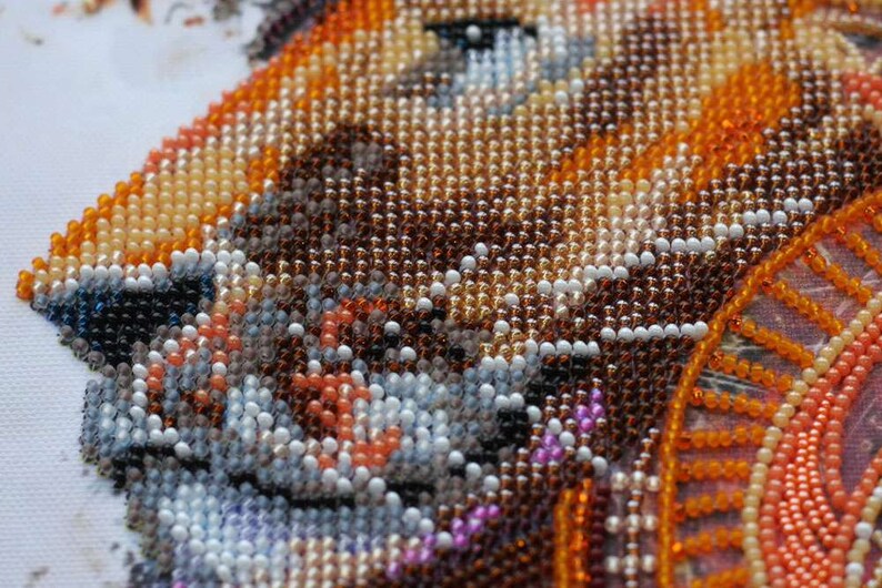 K&ouml;nnte beinhalten: Nahaufnahme eines Perlenbildes, das einen Fuchs mit orangefarbenen, braunen und wei&szlig;en Perlen darstellt. Das Gesicht des Fuchses ist scharf, der Hintergrund ist ein verschwommener Bereich aus orangefarbenen und braunen Perlen.