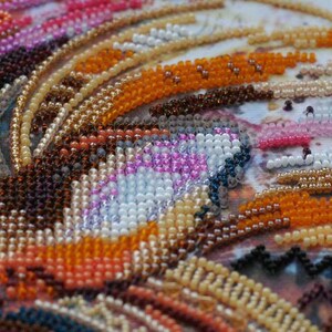 K&ouml;nnte beinhalten: Nahaufnahme eines Perlenkunstwerks mit einem wirbelnden Muster aus orangefarbenen, braunen, wei&szlig;en, rosa und blauen Perlen.