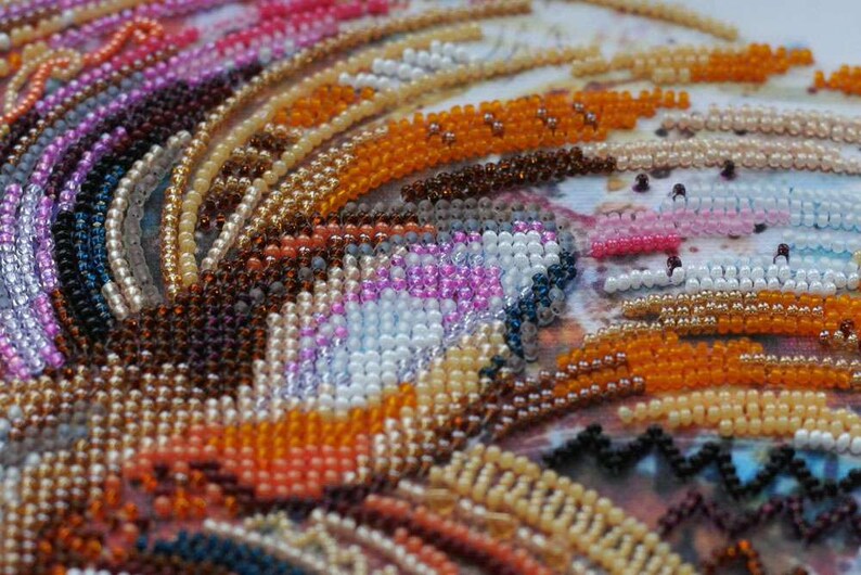 K&ouml;nnte beinhalten: Nahaufnahme eines Perlenkunstwerks mit einem wirbelnden Muster aus orangefarbenen, braunen, wei&szlig;en, rosa und blauen Perlen.