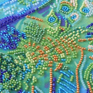 K&ouml;nnte beinhalten: Nahaufnahme eines Perlenkunstwerks mit einem Farbschema in Blau, Gr&uuml;n und Orange. Die Perlen sind in einem wirbelnden Muster angeordnet, das ein Gef&uuml;hl von Bewegung und Tiefe erzeugt.