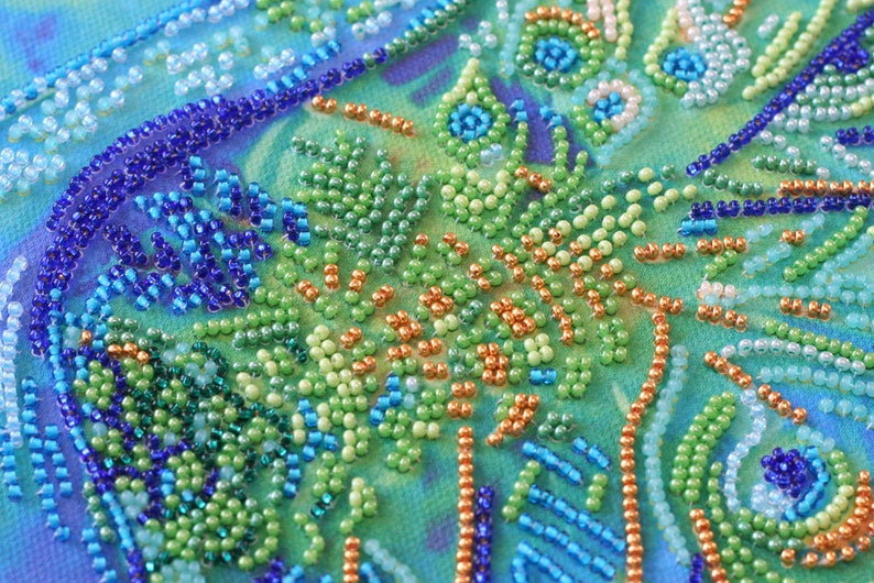 K&ouml;nnte beinhalten: Nahaufnahme eines Perlenkunstwerks mit einem Farbschema in Blau, Gr&uuml;n und Orange. Die Perlen sind in einem wirbelnden Muster angeordnet, das ein Gef&uuml;hl von Bewegung und Tiefe erzeugt.