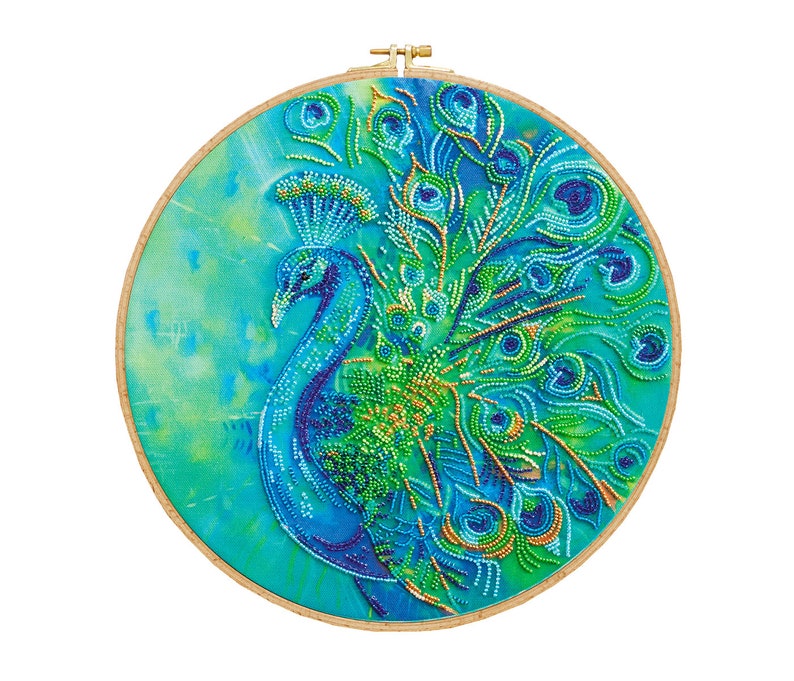 K&ouml;nnte beinhalten: Ein runder Stickrahmen mit einem Pfauenmotiv. Der Pfau ist aus blauen, gr&uuml;nen und goldenen Perlen gefertigt. Der Hintergrund ist ein hellblauer und gr&uuml;ner Aquarell-Wasch.