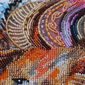 K&ouml;nnte beinhalten: Nahaufnahme eines Perlenkunstwerks mit einer Vielzahl von Farben, darunter Orange, Braun, Wei&szlig; und Rosa. Die Perlen sind in einem Muster angeordnet, das einen wirbelnden Effekt erzeugt.
