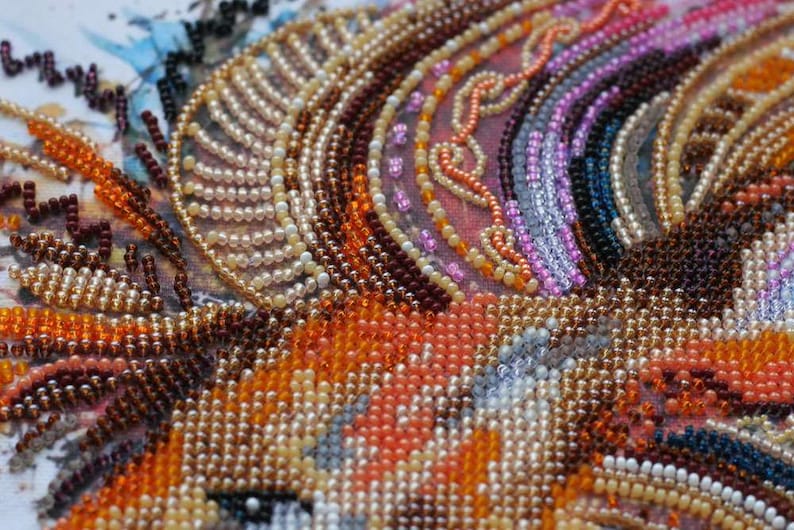 K&ouml;nnte beinhalten: Nahaufnahme eines Perlenkunstwerks mit einer Vielzahl von Farben, darunter Orange, Braun, Wei&szlig; und Rosa. Die Perlen sind in einem Muster angeordnet, das einen wirbelnden Effekt erzeugt.