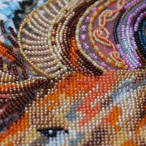 K&ouml;nnte beinhalten: Nahaufnahme eines Perlenkunstwerks mit einer Vielzahl von Farben, darunter Orange, Braun, Wei&szlig; und Rosa. Die Perlen sind in einem Muster angeordnet, das ein strukturiertes und kompliziertes Design erzeugt.