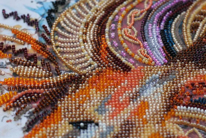 K&ouml;nnte beinhalten: Nahaufnahme eines Perlenkunstwerks mit einer Vielzahl von Farben, darunter Orange, Braun, Wei&szlig; und Rosa. Die Perlen sind in einem Muster angeordnet, das ein strukturiertes und kompliziertes Design erzeugt.