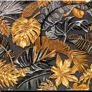 Könnte beinhalten: Eine schwarze Leinwand mit einem Perlenmuster aus goldenen und silbernen tropischen Blättern. Die Blätter sind in einem zufälligen Muster angeordnet und erzeugen einen strukturierten Effekt.
