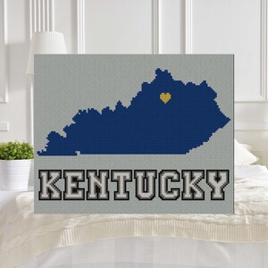 May include: A cross-stitch pattern of the state of Kentucky with a yellow heart in the center. The word "KENTUCKY" is stitched in gray below the state outline.