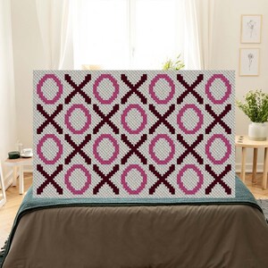 May include: A rectangular headboard with a tic-tac-toe pattern. The design features alternating rows of pink circles and dark burgundy X's on a light gray background. The headboard is placed on a bed with a brown comforter and a teal blanket.