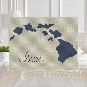 Puede incluir: Un diseño de punto de cruz azul marino de las islas hawaianas con la palabra "love" bordada debajo. El diseño está en una tela beige.