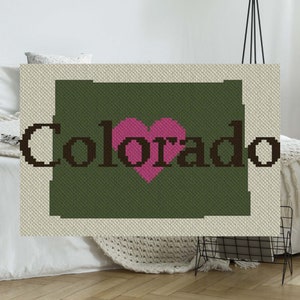 May include: A green and white crocheted blanket with the word "Colorado" and a pink heart in the center.