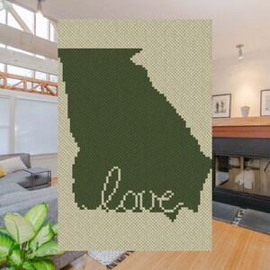 May include: A green crochet wall hanging in the shape of the state of Georgia with the word "love" written in white inside the state outline.