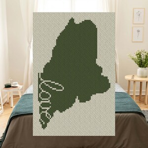 May include: A green crochet blanket with the state of Maine outlined in green and the word "Maine" written in white.