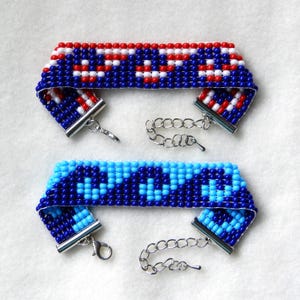 May include: Two beaded bracelets with silver clasps. The top bracelet is red, white, and blue. The bottom bracelet is blue and turquoise.