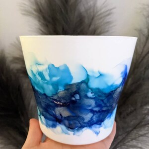 May include: White ceramic planter with a blue and silver abstract design. The design resembles watercolours or ink.