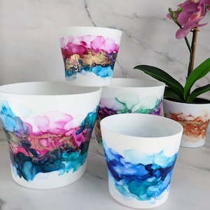 May include: Set of four white ceramic planters with abstract watercolour designs in shades of pink, blue, green, and gold. The planters are of varying sizes and are arranged in a staggered formation.