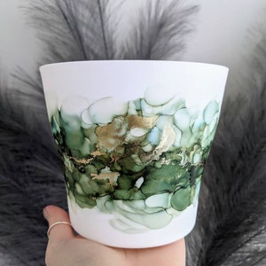 May include: White ceramic planter with a green and gold abstract design. The design features swirling patterns and gold accents.