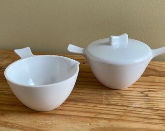 May include: A white ceramic creamer and sugar bowl set. The creamer has a spout and a handle. The sugar bowl has a lid with a small handle.