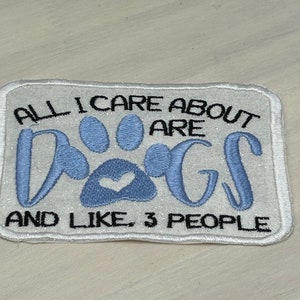 May include: White embroidered patch with blue paw print and the text "All I care about are dogs and like, 3 people."
