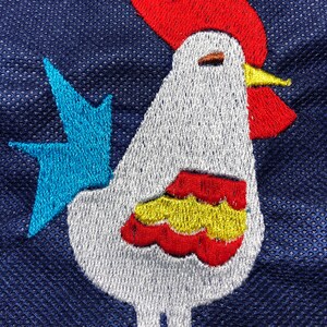 May include: Embroidered white rooster with a red comb and wattle, yellow beak, and blue tail feathers. The rooster is on a dark blue background.