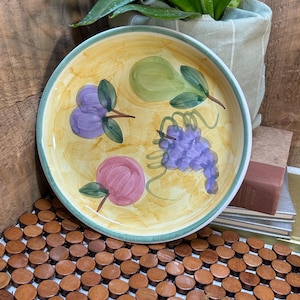 May include: A white ceramic mug with a black handle and the text "But First, Coffee" in a bold, black font. The mug is set against a blurred background, suggesting a cozy setting.