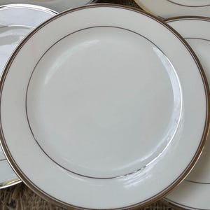 May include: A set of white ceramic plates with a thin gold rim. The plates are stacked on top of each other.