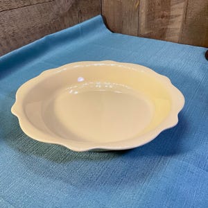 May include: A round, pale yellow ceramic pie dish with a smooth, glossy finish and a decorative scalloped edge. The dish features a shallow basin and a wide, curved rim, providing a clean, uniform appearance for baking and serving various food items.