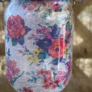 May include: A glass jar with a floral pattern, a silver lid, and a silver hanging loop. The jar is filled with a white substance.