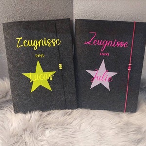Peut inclure: Deux dossiers en feutre gris avec des étoiles roses et jaunes et le texte "Zeugnisse von" suivi des noms "Lucas" et "Julie".
