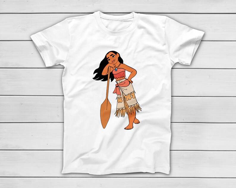 Puede incluir: Camiseta blanca con una ilustraci&oacute;n de dibujos animados de una mujer con un atuendo de inspiraci&oacute;n nativa americana. El personaje est&aacute; apoyado en una paleta de madera. La mujer lleva un top color coral, una falda con flecos y un collar.