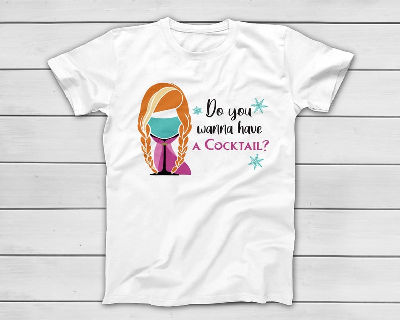 May include: White t-shirt with a graphic of a woman's face with orange hair in braids, a cocktail glass, and the text "Do you wanna have a Cocktail?" in black and purple. Two blue snowflakes are also included in the design.