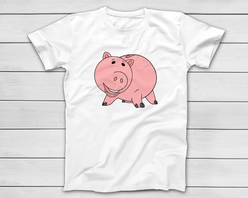 Puede incluir: Camiseta blanca con una ilustraci&oacute;n de dibujos animados de un cerdo rosa con contornos negros. El cerdo est&aacute; sonriendo y de pie sobre sus cuatro patas. El dise&ntilde;o est&aacute; centrado en la parte delantera de la camiseta.