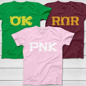 Peut inclure: Trois t-shirts, vert, bordeaux et rose. Le t-shirt vert porte l'inscription "OK" en jaune, le t-shirt bordeaux "ROR" en jaune et le t-shirt rose "PNK" en blanc. Tous les t-shirts sont à manches courtes.
