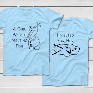 以下が含まれることがあります： 2つの水色のTシャツ。片方には「A GIRL WORTH MELTING FOR」の文字と漫画の雪だるまが描かれています。もう片方には「I MELTED FOR HER」の文字と溶けた雪だるまが描かれています。
